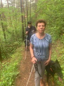 V krásnom lesnom prostredí sa prechádza skupinka účastníkov s bielou palicou