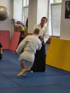 V aikido úbore predvádzajú inštruktori ako správne padať. Na fotke jeden muž drží druhého za pažu a telo druhého muža je v pozícii pomalého klesania ku zemi